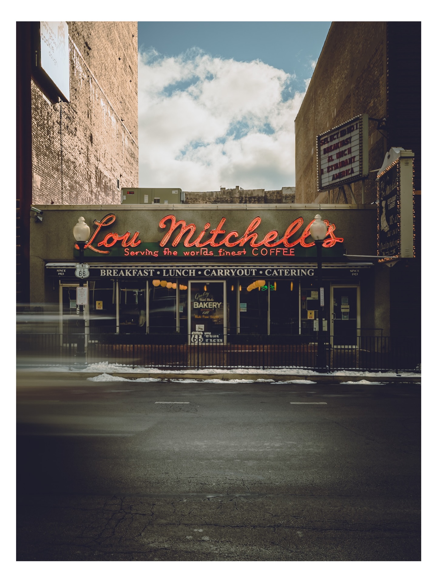 Lou Mitchell’s neon sign beneath a patch of blue sky, with snow still along the sidewalk.