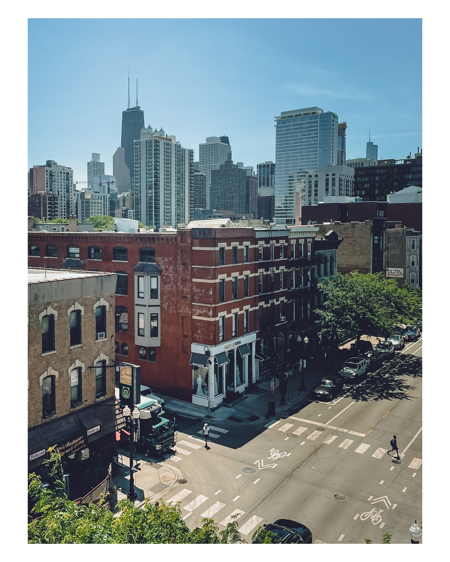 Neighborhood storefronts and a sunlit intersection, with the skyline rising behind Old Town.